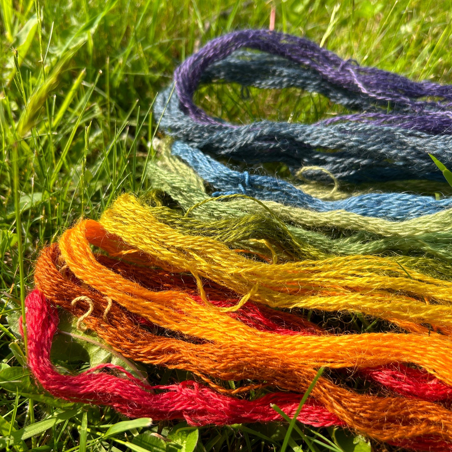 Colorful naturally dyed wool embroidery floss on a grassy background