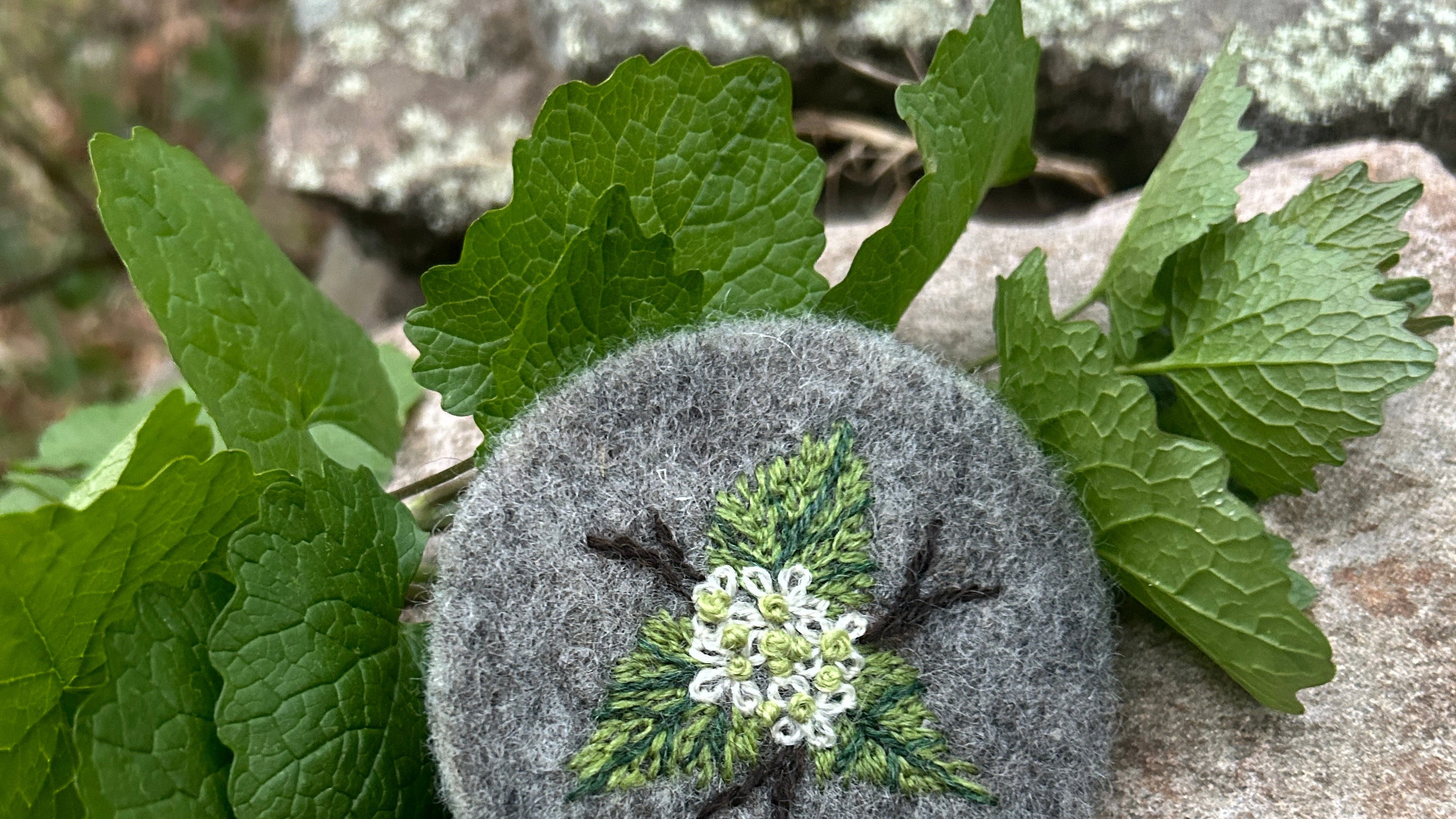 Round gray felt badge with garlic mustard on a textured stone surface