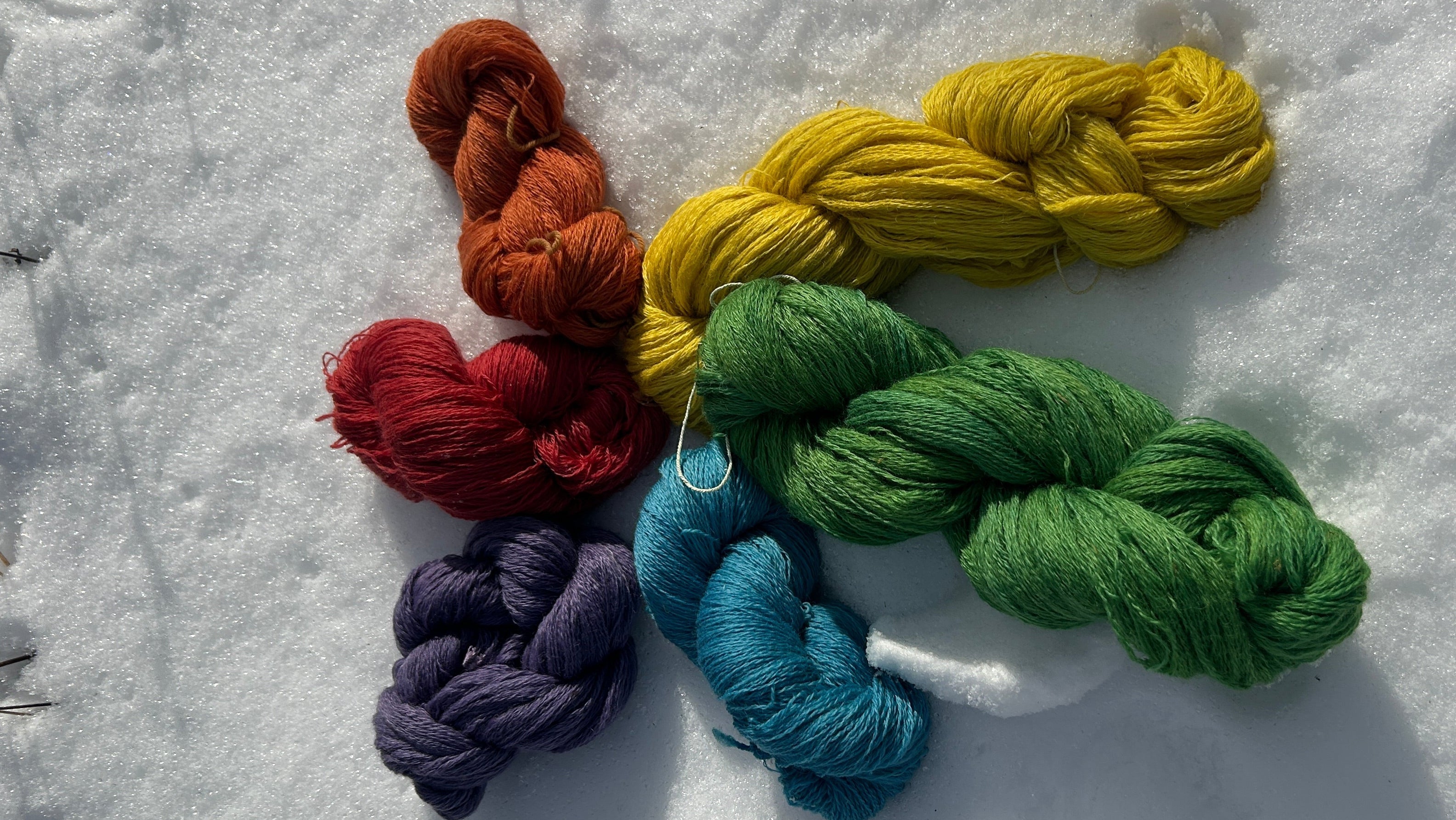 Colorful yarn skeins arranged in a flower pattern on snow