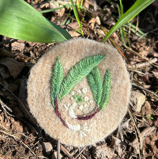 Round tan felt badge with embroidered design of ramps sitting in front of a ramp plant.